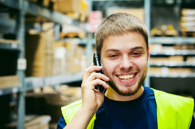 Portrait of smiling man holding camera while standing in factory