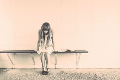 Woman sitting on seat against wall