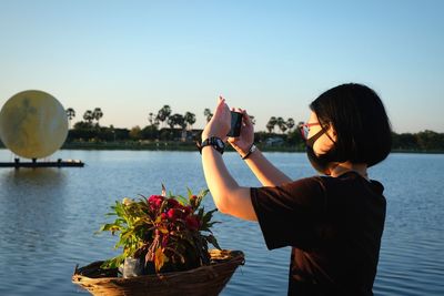 Man photographing by lake against clear sky