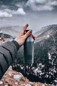 Hand holding snow covered mountain against sky