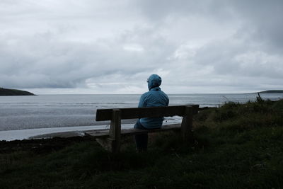 Rear view of woman sitting on bench by sea against sky