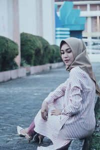 Side view of woman wearing hijab while sitting against buildings