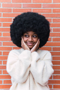 Portrait of young woman with curly hair standing against brick wall