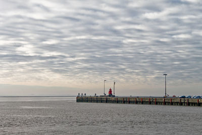 Light house by sea against cloudy sky