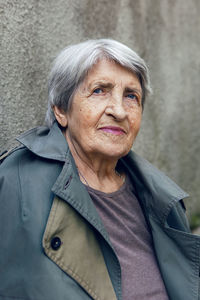 Portrait of an old siniors grandmother of 90 with gray hair stands against a gray wall on the street