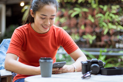Mid adult woman using mobile phone while sitting on table