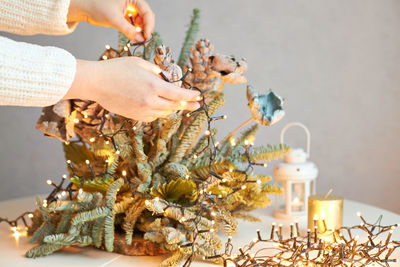 The girl's hands decorate the christmas decoration from fir branches with a garland of lights.