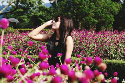 Woman wearing sunglasses while standing amidst pink flowers in garden