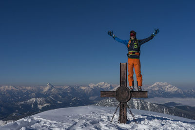 Hiker with arms outstretched standing on metallic structure against sky during winter