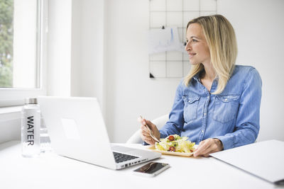 Smiling businesswoman eating food while sitting in office