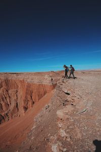 Man photographing through camera with friend while standing on cliff against blue sky