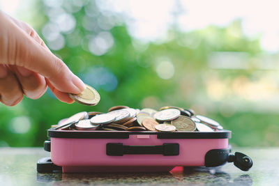 Close-up of hand holding coin over toy luggage