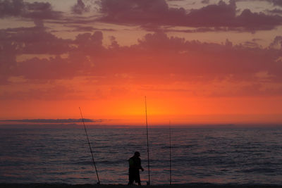 Silhouette man fishing in sea at sunset