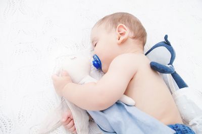 High angle view of shirtless baby boy with pacifier and toy sleeping on bed at home