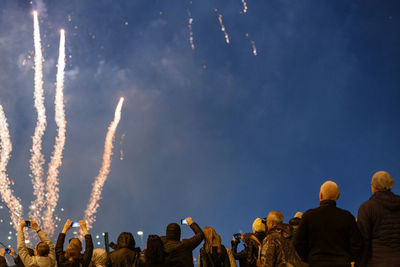 View from the back at people in wark clothes shooting fireworks on the phone at cold night.