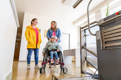 Mother and child living with cerebral palsy using wheelchair lift to access public building.