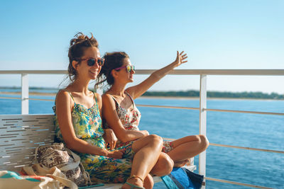 Young woman sitting by sea against sky