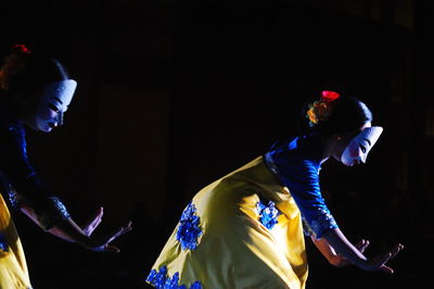 Side view of women with mask dancing on stage