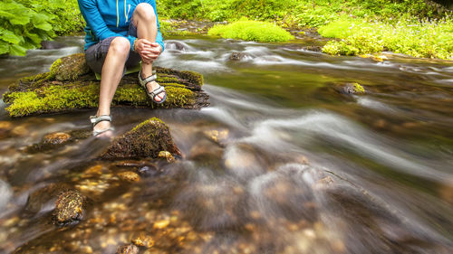 Low section of person standing on rock by stream