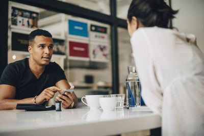 Businessman talking to colleague and using mobile phone while doing blood sugar test while sitting at table in office