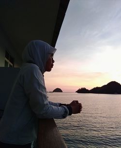 Side view of woman looking at sea against sky during sunset