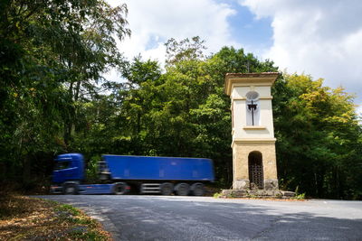 Road by trees and building against sky