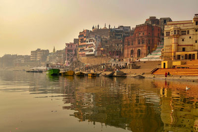 Buildings by river against sky during sunset