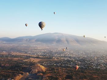 Hot air balloons flying in city against clear sky