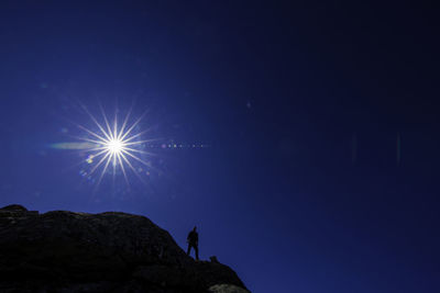 Low angle view of man standing on mountain against clear blue sky on sunny day
