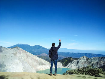 Rear view of man standing on mountain against blue sky