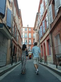 Rear view of man and woman walking on street amidst buildings in city