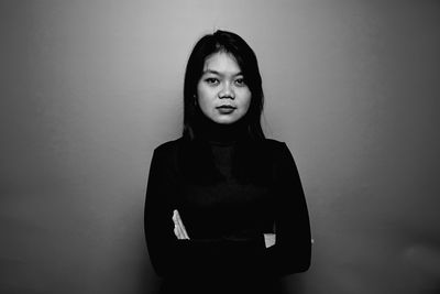 Portrait of young woman standing against wall