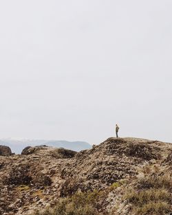 Rear view of man standing on cliff against clear sky