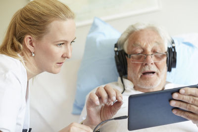 Female nurse assisting senior man in using digital tablet on hospital bed