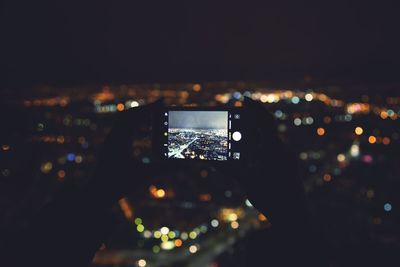 Close-up of hand photographing illuminated cityscape at night
