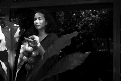 Woman holding artificial fruit decoration while standing by window