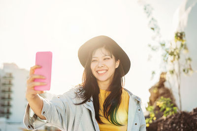 Smiling woman wearing hat taking selfie standing outdoors