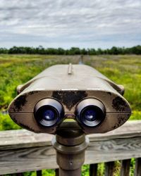 Close-up of coin-operated binoculars on field against sky