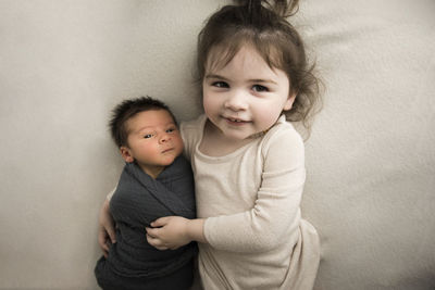 Big sister hugs newborn baby brother while laying on white blanket