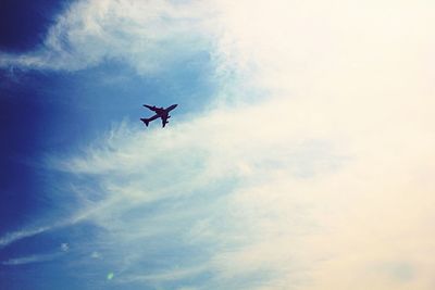 Low angle view of silhouette airplane against cloudy sky