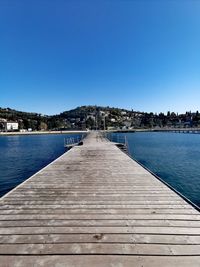 Pier over sea against clear blue sky