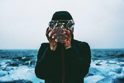 Man holding umbrella against sea