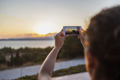 Woman taking a photo with her mobile phone at sunset