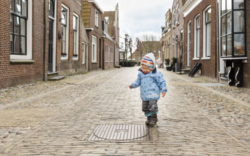 Full length of baby girl walking on footpath amidst buildings