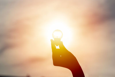 Silhouette person holding sun against sky during sunset