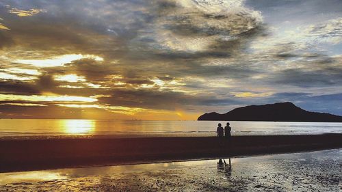 Silhouette people on beach against sky during sunset