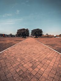 Empty footpath by street in city against sky