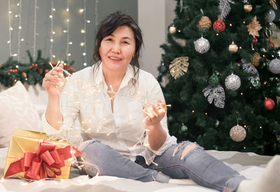 Portrait of young woman sitting on christmas tree at home