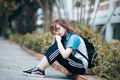 Young woman looking away while sitting on plant