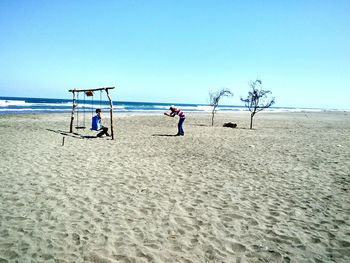 People at beach against clear blue sky